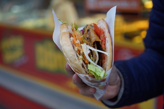 Frischer Döner Kebab mit Fleisch, Salat und Gemüse in der Hand serviert als Streetfood